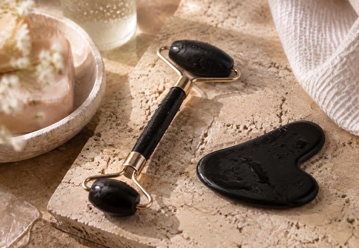 Black face roller and heart gua sha on a travertine tray